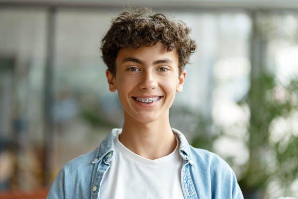 Closeup portrait of smiling smart curly haired school boy wearing braces on teeth looking at camera. Education concept